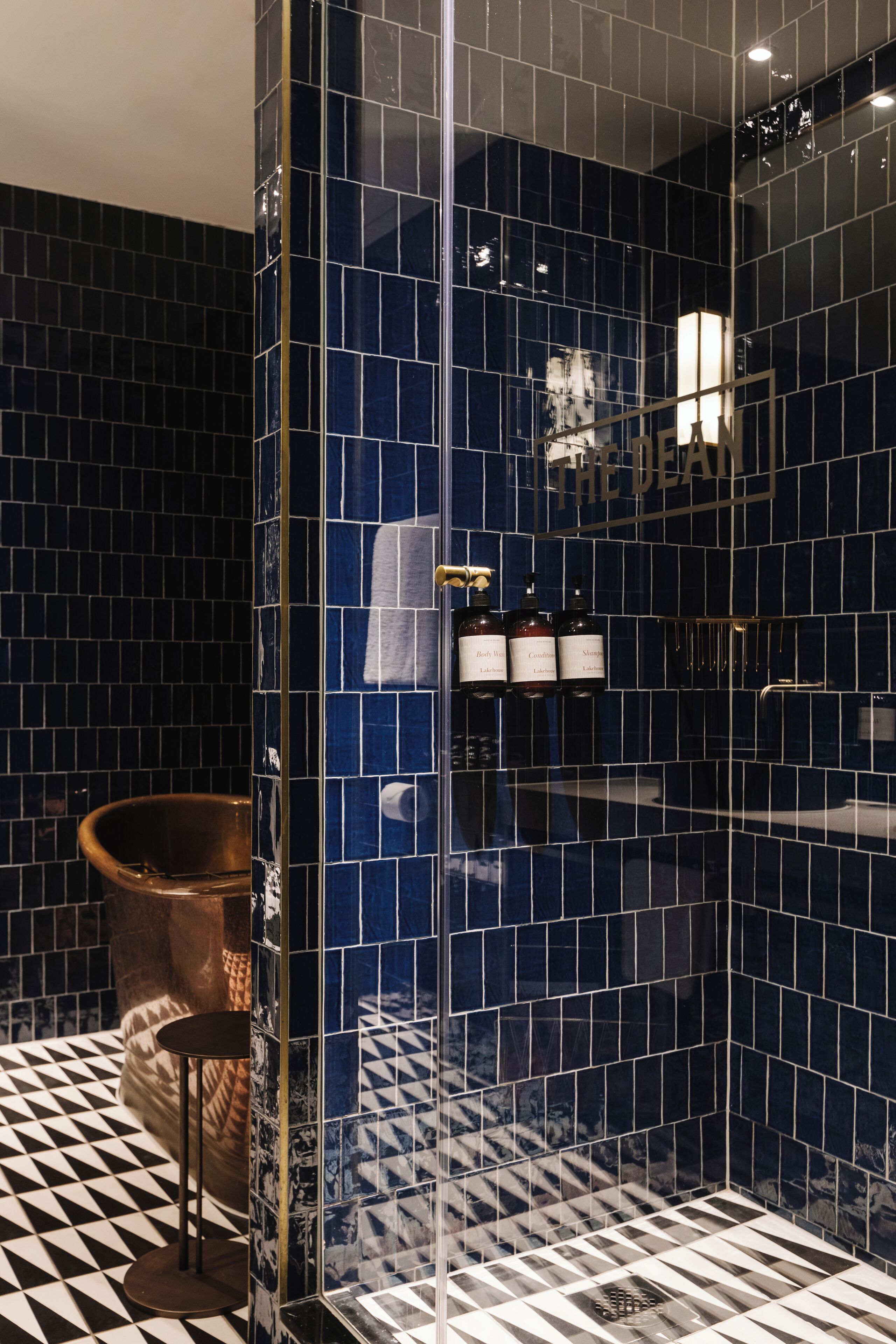 Un baño moderno con paredes de azulejos azul oscuro, piso a cuadros blanco y negro, y zona de ducha con mampara de vidrio.