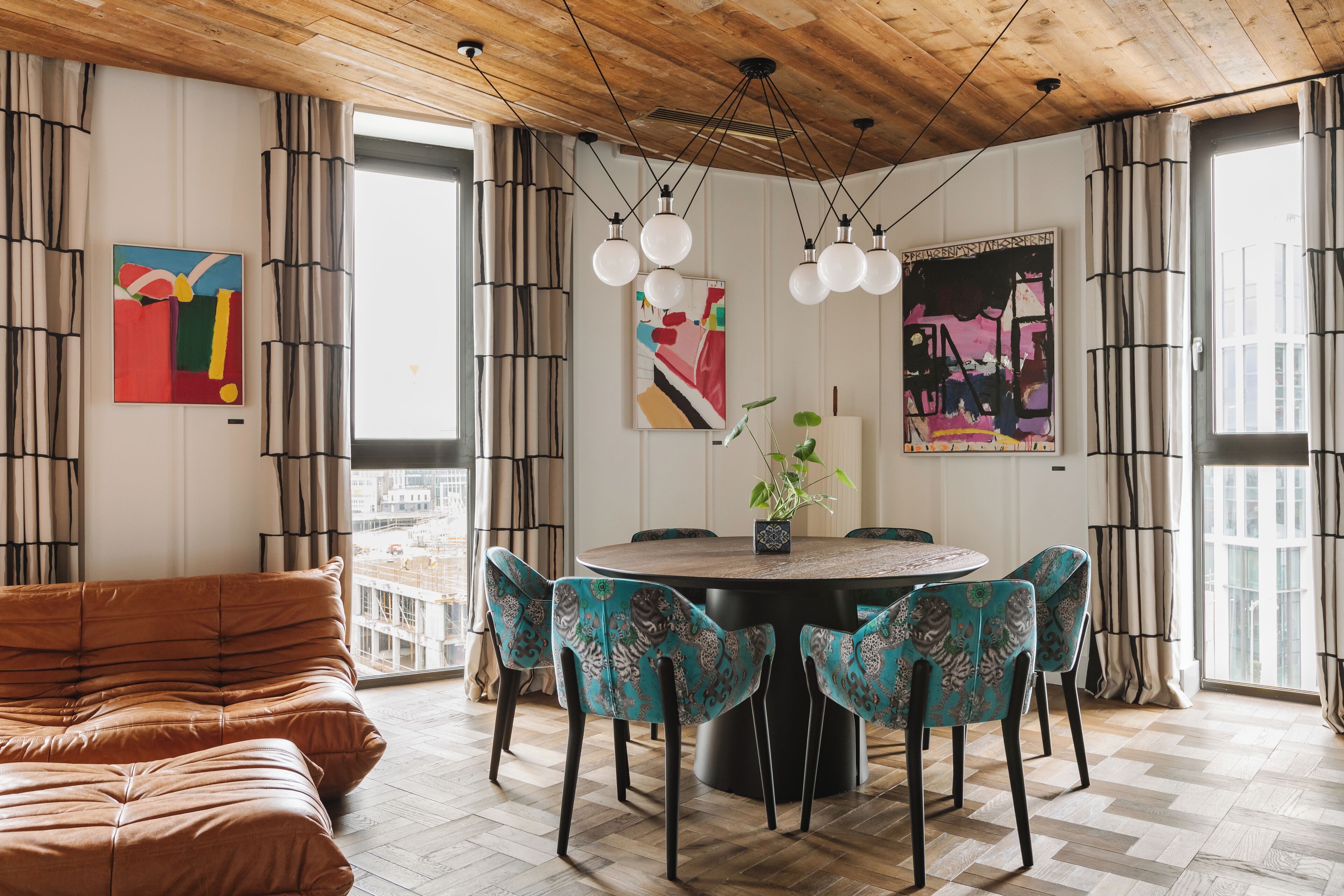 A dining area with a round table, four chairs, and a brown sofa.