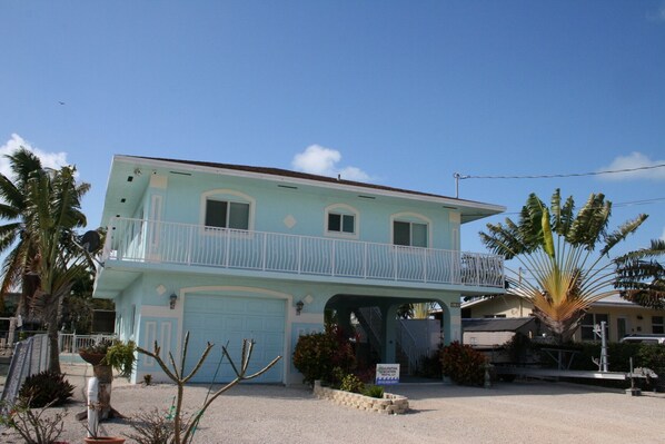 A two-story building with a light blue exterior, a balcony on the second floor, and a garage.
