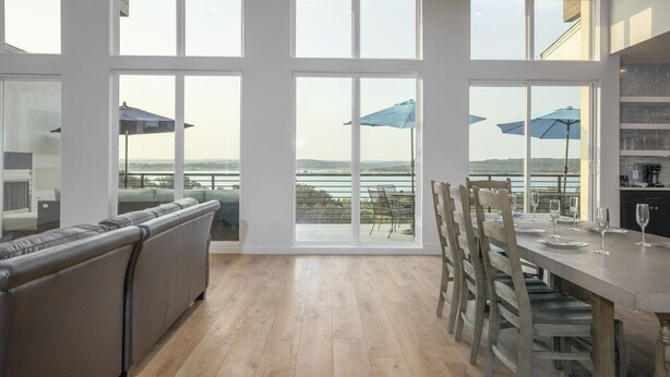 A spacious room with large windows, a dining area, and a view of the water. - The Oasis at Canyon Lake - Gorgeous & Modern Waterfront Home + Pool + Sweeping Lake Views (Canyon Lake)