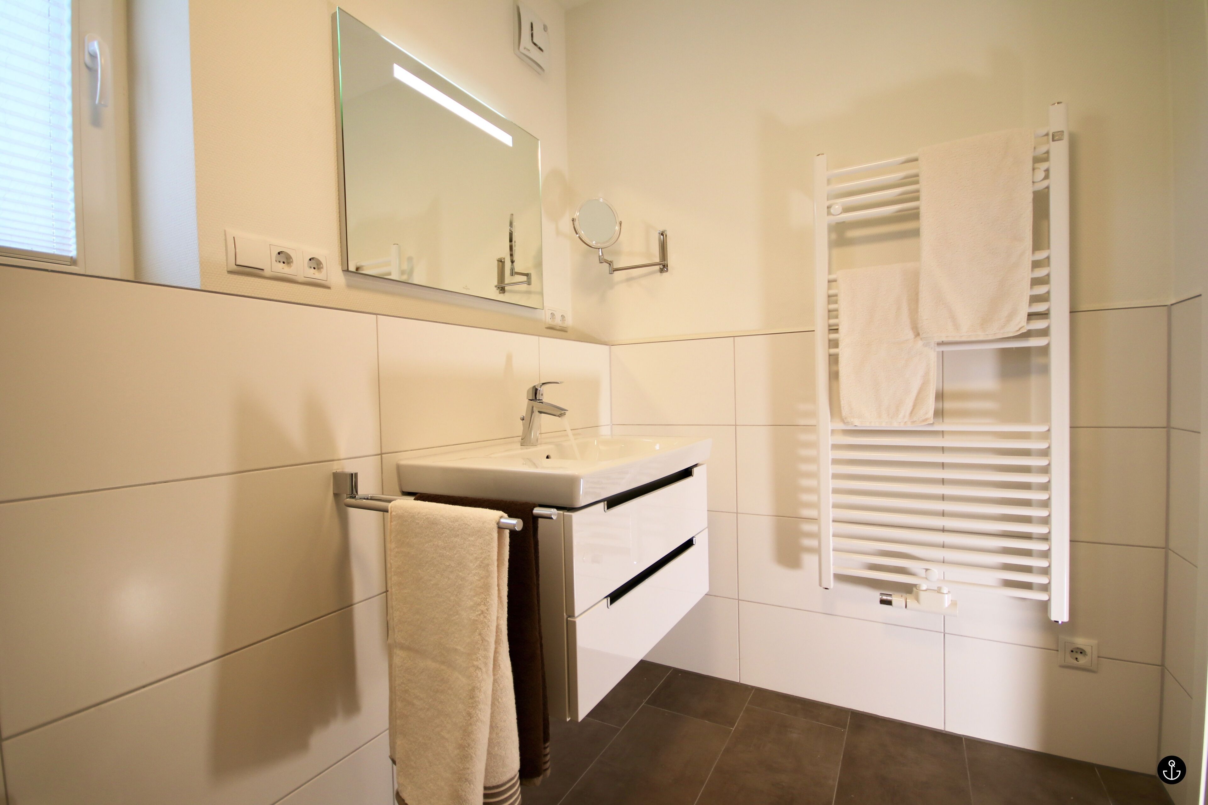 A bathroom with a sink, mirror, towel rack, and a towel warmer.