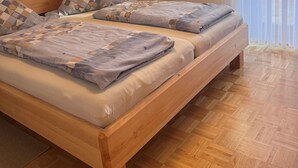 Een tweepersoonsbed met een geruit dekbed en kussens, een houten hoofdbord en een houten vloer.