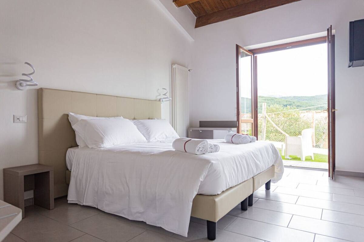 A bedroom with a bed, bedside tables, a radiator, and a view of the outdoors.