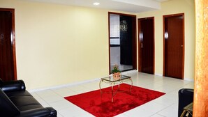 Un vestíbulo de hotel con alfombra roja, una mesa de centro de vidrio y sofás de cuero negro.