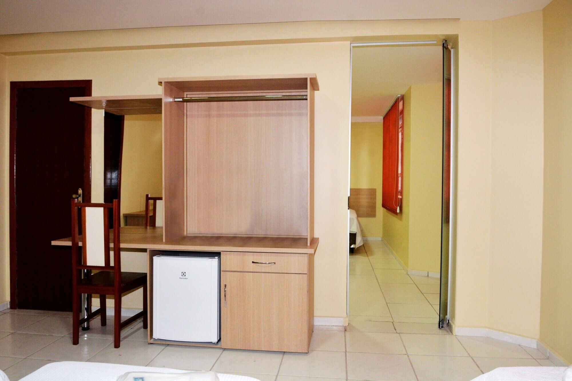 A compact room with a wooden desk, a small refrigerator, and a chair.