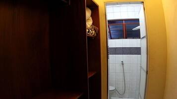 A small, narrow bathroom with a shower, tiled walls, and wooden shelves.