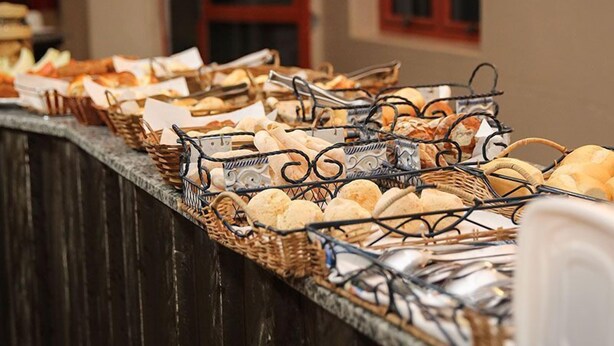 Mostrador de buffet con diferentes panes y pasteles exhibidos en cestas.