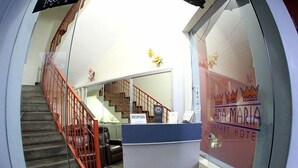 Un mostrador de recepción con un letrero que dice "RECEPCAO" y un muro de cristal con la señalización "ANA MARIA APA ART HOTEL".