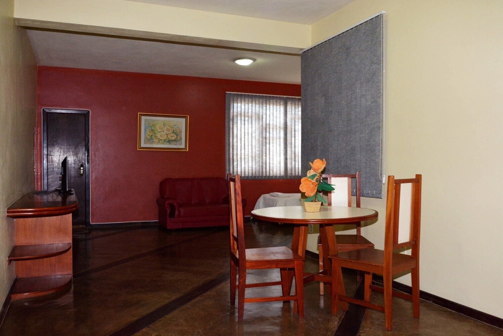 Zona pranzo con tavolo rotondo, sedie in legno, un divano rosso e un quadro appeso al muro.