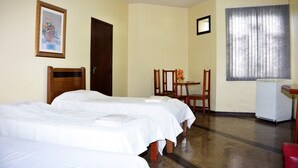 Habitación de hotel con dos camas, un escritorio, una silla, un refrigerador y una ventana con cortinas.