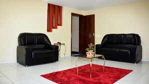 Una habitación con dos sofás de cuero negro, una mesita con una planta y una alfombra roja sobre suelo de baldosas.