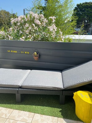 Un banc sur lequel est posé un panier en métal contenant une plante, le tout entouré de verdure et de fleurs.