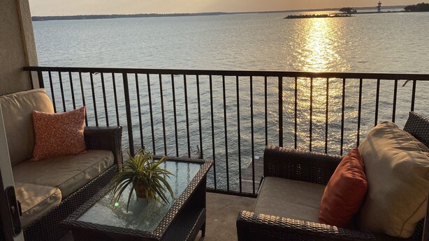 A balcony with wicker furniture and a glass table, overlooking a calm body of water with a distant lighthouse. - Lake house - unit 309 (Willis)