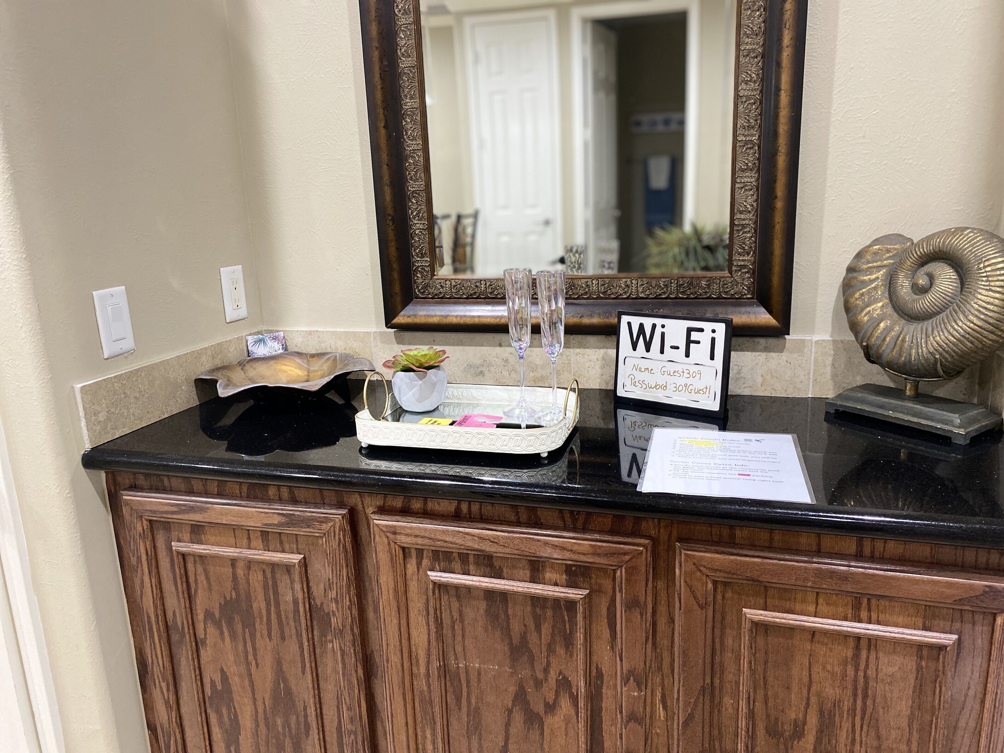 Zona de recepció d'hotel amb un taulell negre, un mirall, un senyal de Wi-Fi, una petita planta i una closca decorativa.