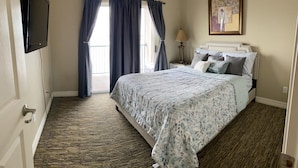 A bedroom with a bed, curtains, a lamp, and a painting on the wall. - Lake house - unit 309 (Willis)