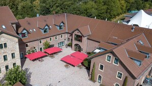 A multi-story building with a courtyard featuring red umbrellas and outdoor seating. - ClassicX Landhaus & Hotel (Gensingen)