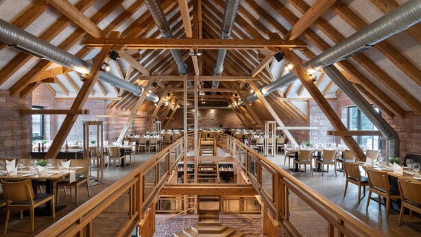 A spacious dining area with high wooden beams and a central staircase. - ClassicX Landhaus & Hotel (Gensingen)