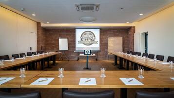 Ein Konferenzraum mit langen Tischen, Stühlen, einer Whiteboard und einer Projektionsleinwand, auf der 'ClassicX Landhaus & Hotel' angezeigt wird.