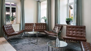 A modern lounge area with leather sofas, a glass coffee table, and potted plants. - ClassicX Landhaus & Hotel (Gensingen)
