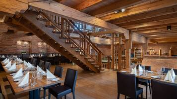 A restaurant with wooden beams, brick walls, and a wooden staircase. Tables are set with white napkins and glasses.