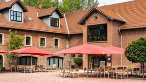 A brick building with a courtyard featuring outdoor seating and umbrellas. - ClassicX Landhaus & Hotel (Gensingen)