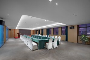 Un salón de conferencias con una larga mesa, sillas blancas y vistas a la ciudad a través de amplias ventanas.