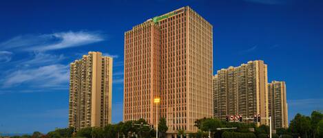 A tall hotel building with a green sign, surrounded by other high-rise buildings and a clear sky.