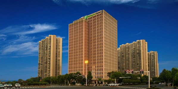 Un edificio de hotel alto con un letrero verde, rodeado de otros edificios de gran altura y un cielo despejado.