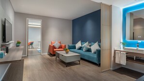 Ein modernes Wohnzimmer mit Sofa, Couchtisch und Fernseher. Es gibt eine Küchenzeile mit Spüle und Schränken.