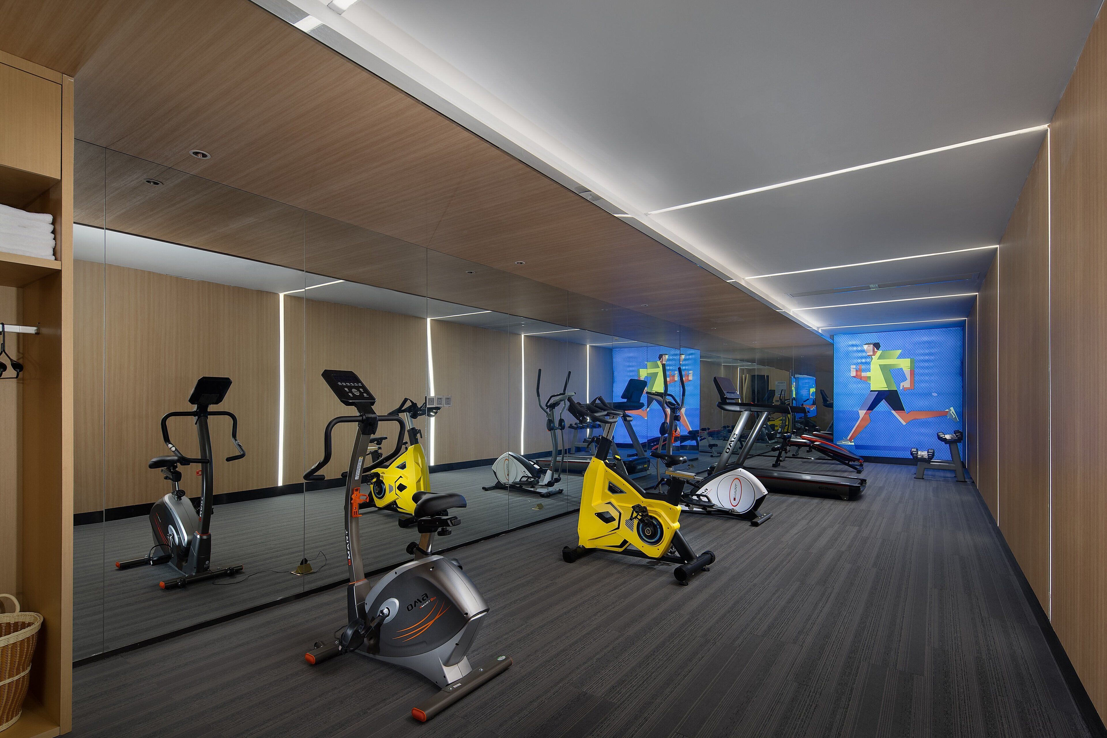 A gym with exercise equipment, mirrors, and a digital screen displaying a running animation.