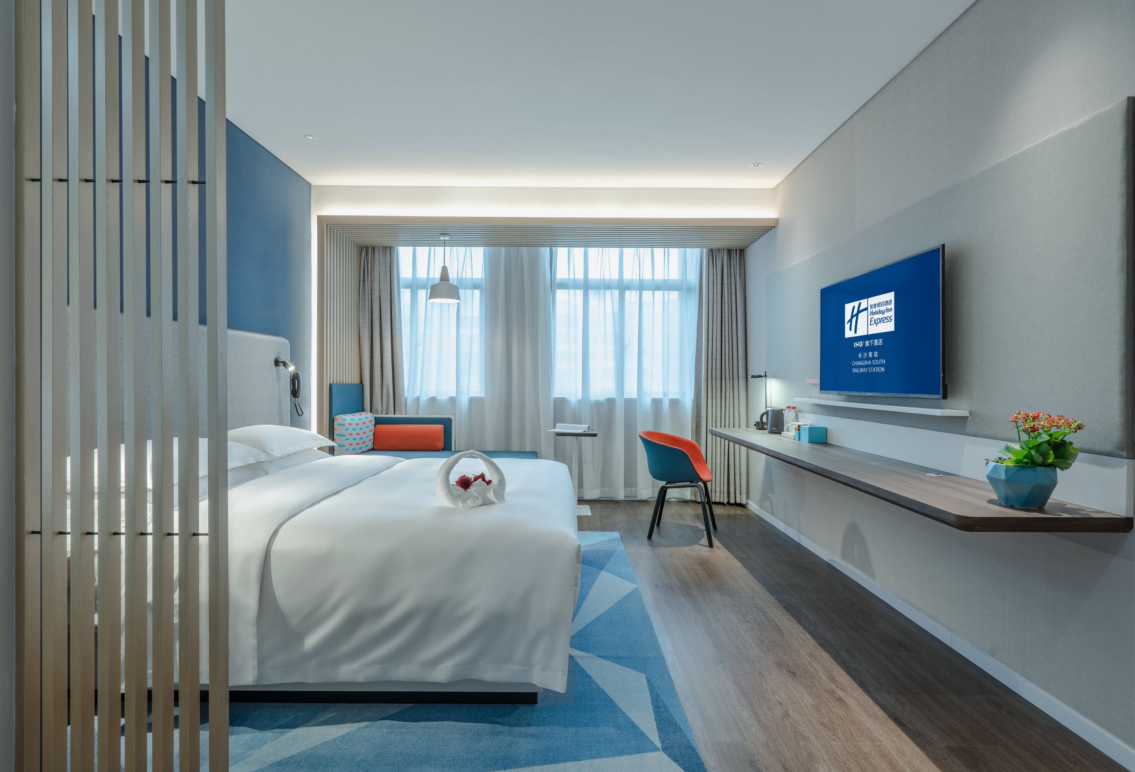 Ein modernes Hotelzimmer mit Bett, Schreibtisch, Stuhl, Fernseher und einem großen Fenster mit Vorhängen.