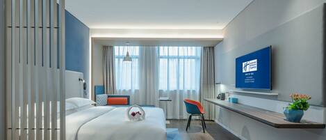 Ein modernes Hotelzimmer mit Bett, Schreibtisch, Stuhl, Fernseher und einem großen Fenster mit Vorhängen.