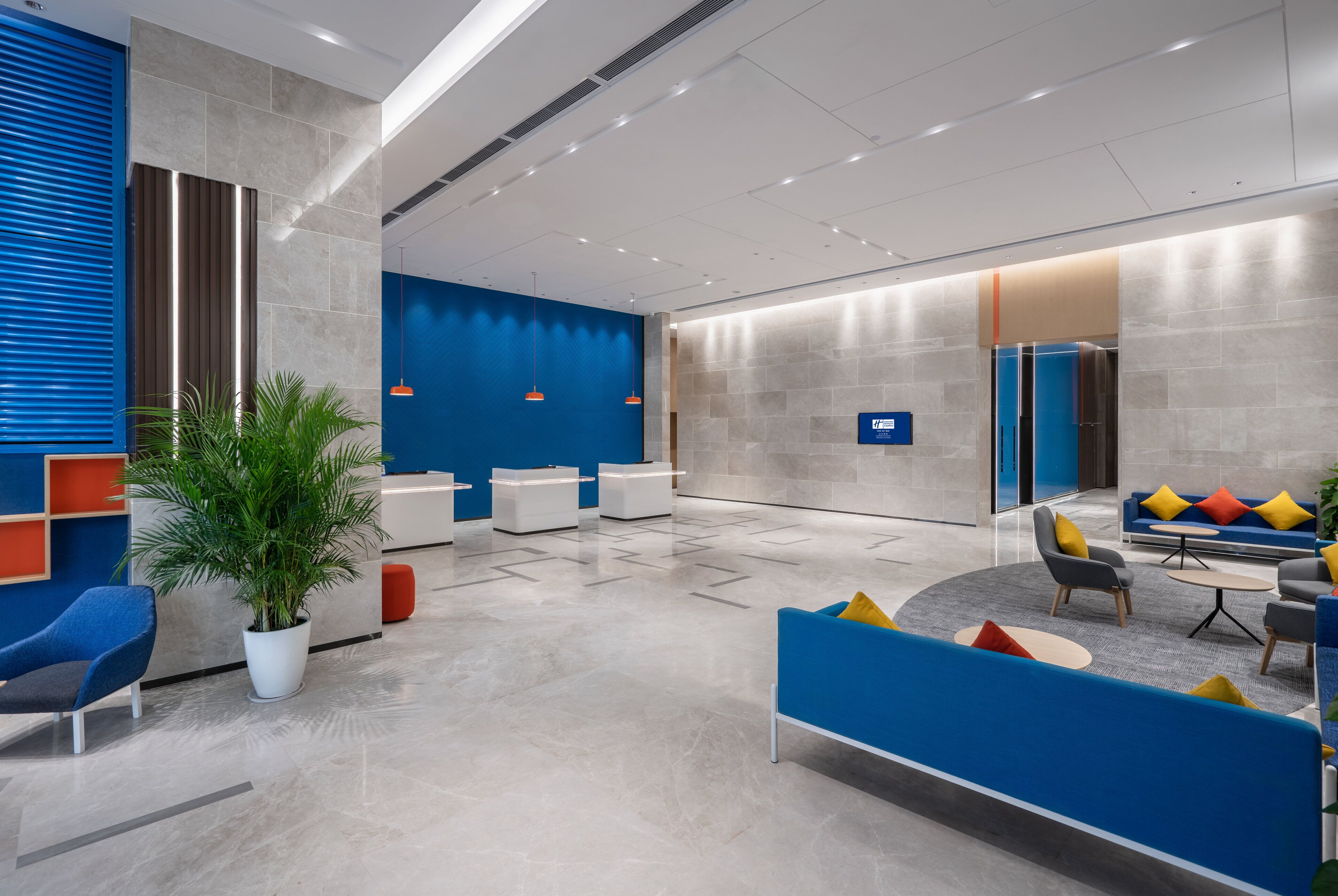 A modern lobby with seating areas, a reception desk, and a blue and grey color scheme.