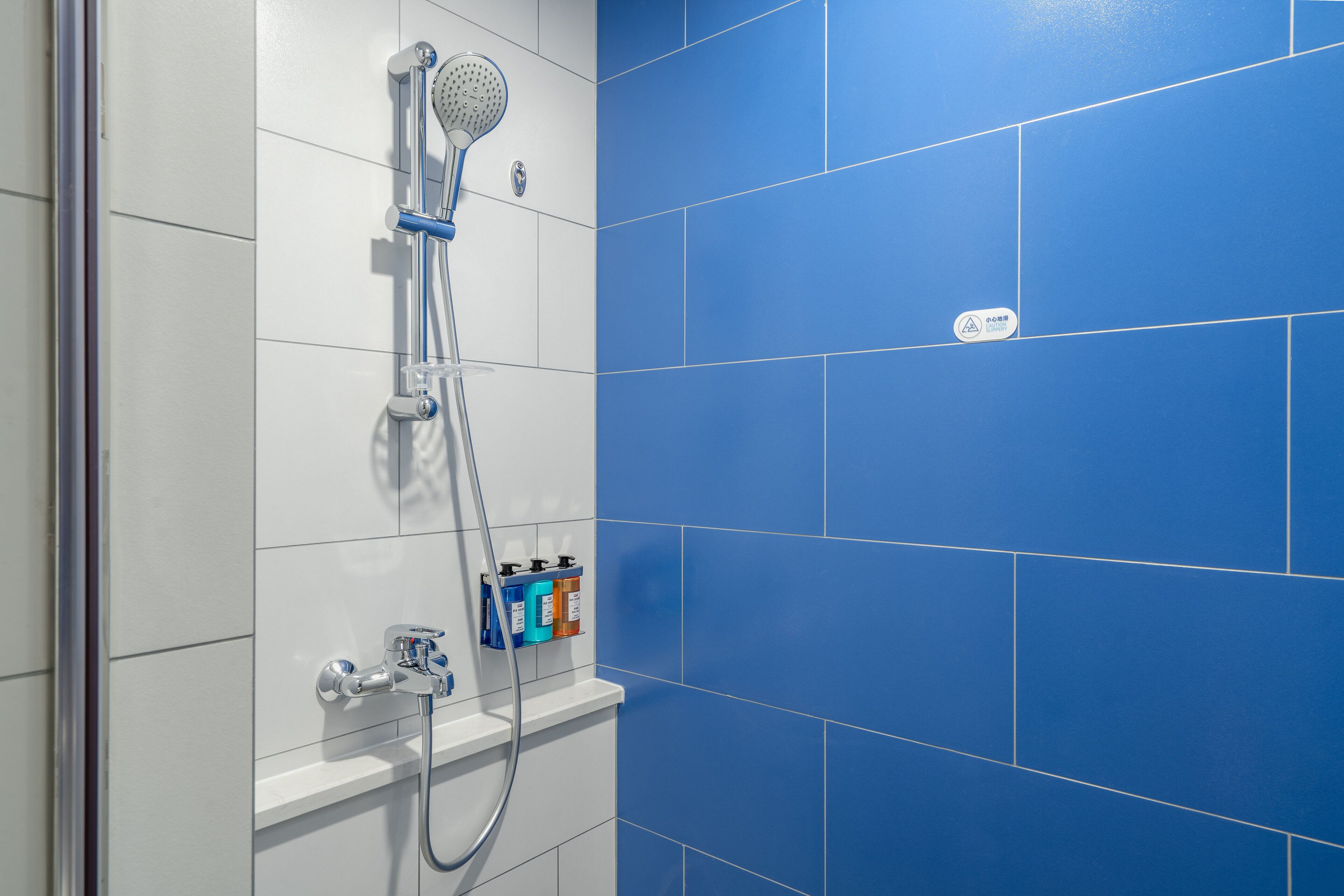 Un baño con ducha, dispensador de jabón en la pared y pared de azulejos azules.