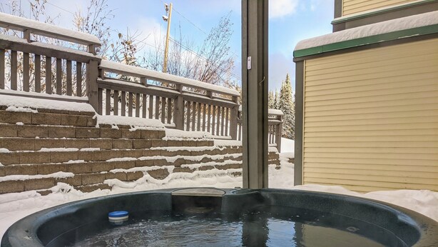 A hot tub in a backyard with snow on the ground and a wooden fence.