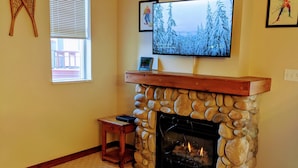 A living room with a stone fireplace, a television mounted above it, and a small wooden table beside the fireplace.