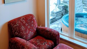 A room with a red patterned armchair, a window with a view of a snowy outdoor area, and a painting of a ski scene.