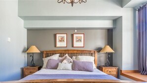 A bedroom with a wooden bed, two bedside tables with lamps, and two framed pictures on the wall.