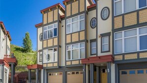 A multi-story residential building with a garage entrance, a covered driveway, and a hillside backdrop.