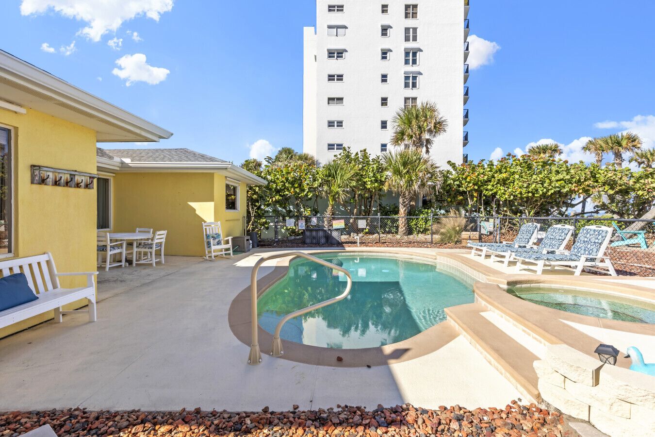 Zona de piscina con sillones reclinables, una pequeña mesa y un edificio al fondo.