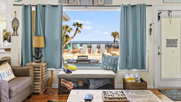 A beach-themed living room with a view of the ocean, a sign reading "SEASIDE", and a bench with a pillow saying "The Beach is my HAPPY". - Seaside Serenity Oceanfront Pool Home (Ormond Beach)
