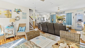 A spacious living room with a large gray sofa, wicker furniture, and a view of the outdoors. - Seaside Serenity Oceanfront Pool Home (Ormond Beach)