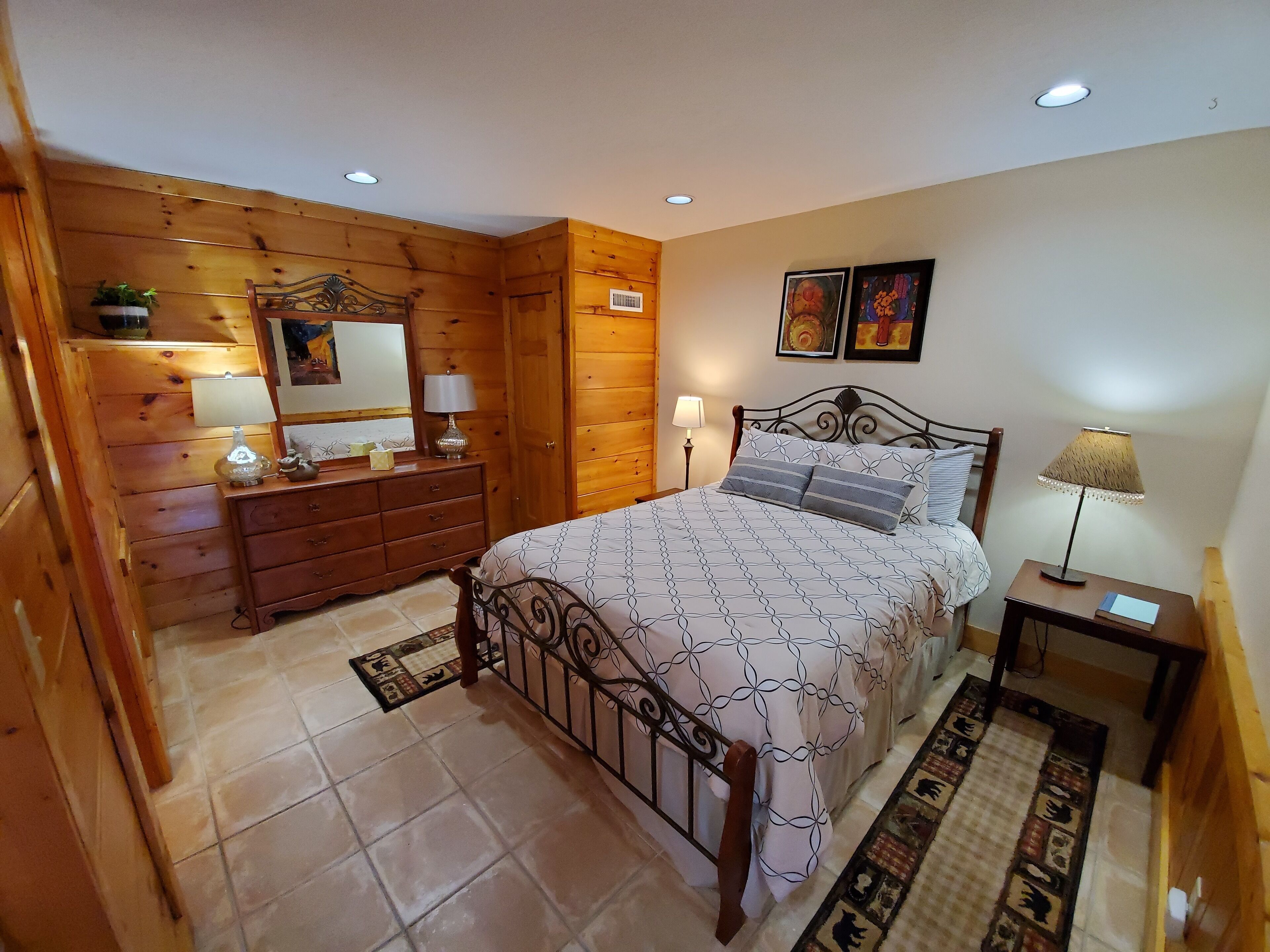 A wooden-paneled bedroom with a bed, dresser, and two bedside lamps.