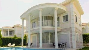 A large, two-story house with a pool, columns, and a balcony.