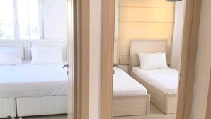 A hotel room with two beds, a window with a curtain, and a hanging light fixture.