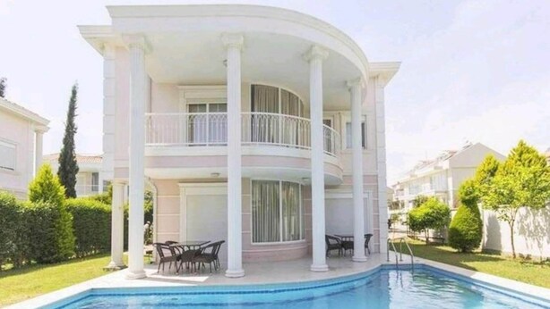 A two-story house with a pool, columns, and a balcony.