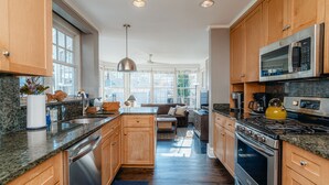 A modern kitchen with granite countertops, stainless steel appliances, wooden cabinets, and a large window providing natural light. - Only Urban Beach House in Chicago (Chicago)
