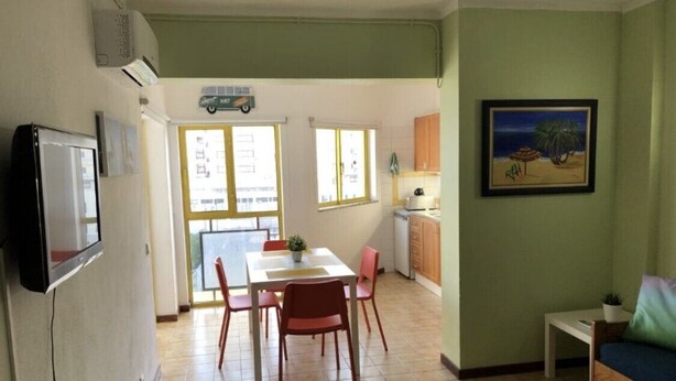 Une cuisine compacte avec un coin repas, une petite table et des chaises. Un téléviseur est fixé au mur, il y a une fenêtre avec vue et un tableau au mur.
