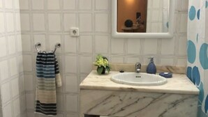 Une salle de bain avec un lavabo en marbre, un porte-serviettes sur lequel est posée une serviette à rayures, une petite plante et un miroir avec une lumière au-dessus.