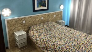 Une chambre à coucher avec une couvre-lit à motifs, un tableau encadré, un climatiseur fixé au mur et un rideau.